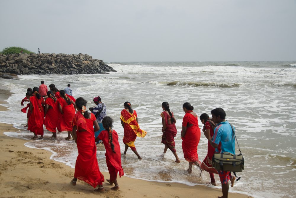 Women in red walk as a group in the surf along Mamallapuram Beach in Chennai